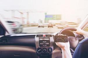 el hombre que conduce un automóvil en la carretera de peaje mientras mira las existencias informa su teléfono móvil peligrosamente foto