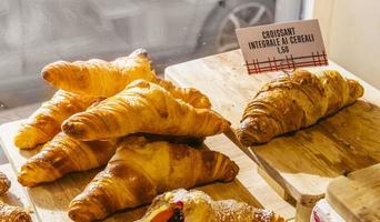 varios sabores de croissant o como en italia se llaman brioche en exhibición en una panadería en milán, italia con un precio y un cartel - albicocca significa mermelada en italiano foto