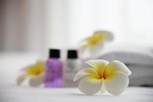 Hotel towel and shampoo and soap bath bottle set on white bed with plumeria flower decorated - relax vacation at the hotel resort concept photo