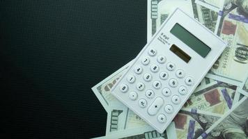 The 100 dollar banknote and calculator on black background for business content photo