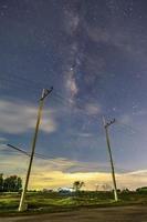 postes eléctricos en el campo nocturno, el cielo con estrellas y hermosas escenas de taro, nubes debajo del horizonte sobre la hierba foto