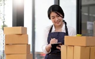 Portrait, entrepreneur, young Asian woman, freelance business, sme business, online shopping, working on laptop computer with parcel box on home office table, online business and delivery concept. photo