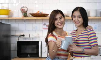 lesbian couple holding coffee mugs in kitchen looking at camera photo