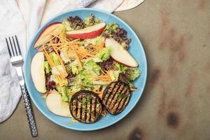 comida saludable ensalada de manzana con berenjena asada lechuga roja en plato tiene tenedor en mesa de madera.