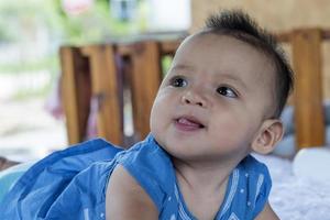 A beautiful 6 month old baby with big eyes lies on the bed. photo