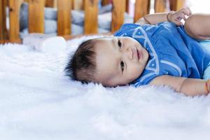 A beautiful 6 month old baby with big eyes lies on the bed. photo