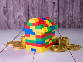 casa de ladrillos de juguete multicolor y monedas de oro para niños o concepto de negocio de propiedad foto