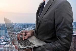 Double exposed of  Businessman holding laptop with cityscape. photo