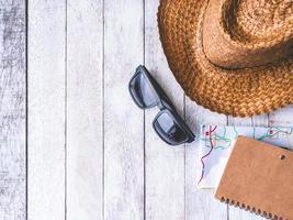 vista superior de gafas de sol, sombrero, cuaderno y mapa sobre mesa de madera. concepto de viaje foto