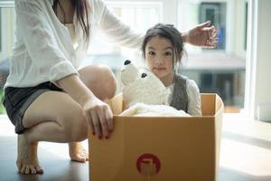 niña asiática feliz jugando con cajas de cartón y su oso, divirtiéndose mientras se muda a un nuevo hogar. foto