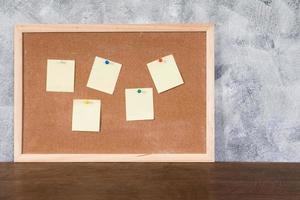 Blank papers pin up on cork board over wooden table with textured background. photo