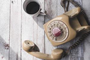 vista superior del teléfono antiguo con taza de café sobre fondo de mesa de madera blanca. foto
