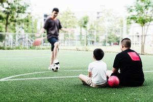 Dad coaches his children how to play soccer or football in green football field - outdoor family sport activity concept photo