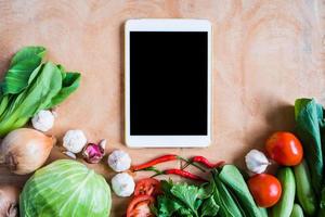 Top view of Fresh vegetables with tablet touch computer gadget on wooden table background. photo