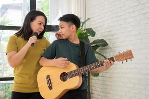 Asian boy playing guitar and mother sing a song and embrace, feel appreciated and encouraged. Concept of a happy family, learning and fun lifestyle, love family ties photo