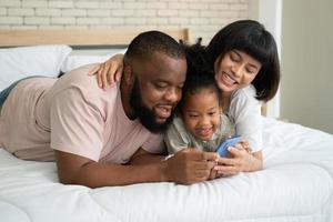 The family has fun and plays education games online with a smartphone at home in the bedroom. Concept of online education and caring from parents. photo