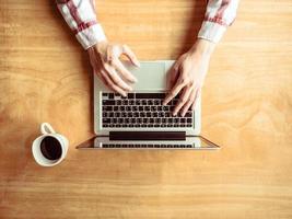 Top view of Male using Laptop with a cup of coffee on wooden table background. photo