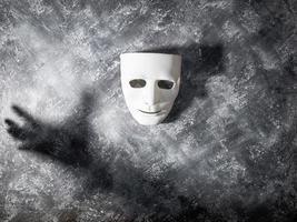 máscara blanca con sombra de mano sobre fondo gris grunge.
