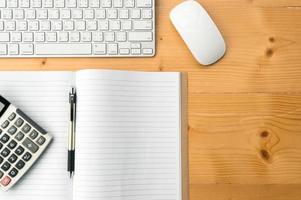 Top view workspace with blank notebook,pen,calculator keyboard and mouse on wooden table background. photo