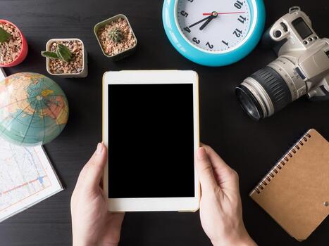 Top view of tablet in hands with camera,cactus,map,globe,clock  and notebook on the office desk. photo