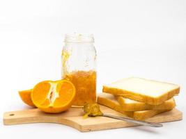 Fresh orange with orange jam in glass jar and  bread on wooden tray over white background. photo