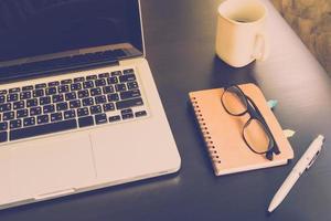 Laptop with cup of coffee,notebook,glasses and pen on the desk, Vintage tone photo