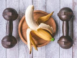 Banana and iron dumbbells on the wooden table background. Workout and Diet concept photo