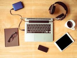 Top view of Electronic devices with notebook, glasses and coffee cup on wooden table background. photo