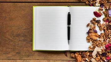 Top view workspace with blank notebook,pen and dried flowers on wooden table background . photo