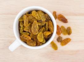 Yellow raisins in cup  on wooden background. photo