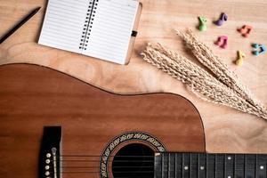 Top view of acoustic guitar with blank notebook on wooden table background. photo