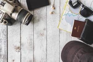 vista superior de la cámara con gorra, gafas de sol, billetera, teléfono inteligente, mapa y pasaporte sobre fondo de mesa de madera blanca, concepto de viaje foto