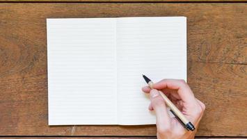 Man hands with pen writing on empty notepad over wooden table. photo