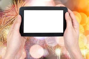 mano masculina sosteniendo un dispositivo de computadora táctil de tableta con pantalla táctil en blanco sobre fuegos artificiales y fondo de luces bokeh. foto