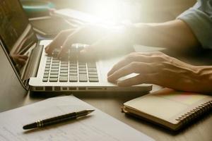 primer plano de las manos masculinas que trabajan en la computadora portátil en su escritorio de oficina, tonificado con la luz del sol. foto