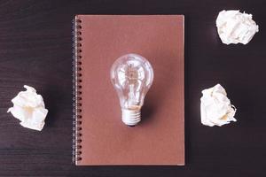 Top view notebook with crumpled paper balls and light bulb on the desk. photo