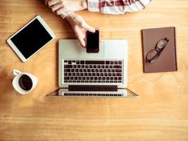 Top view of Male using smart phone with laptop and tablet on wooden table background. photo