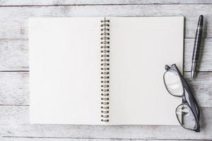 Top view of Notebook with pen and glasses on white wooden table background. photo