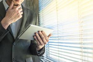 Close up of businessman using tablet device while standing at a window in an office photo