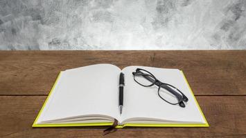 Blank notebook with pen and glasses on wooden table. photo