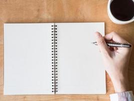 Man hands with pen writing on empty notepad over wooden table. photo