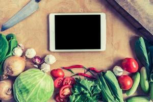 Top view of Fresh vegetables with tablet touch computer gadget on wooden table background. photo