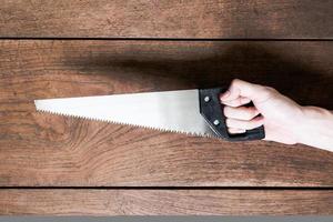 Hand holding saw on wooden table background. photo