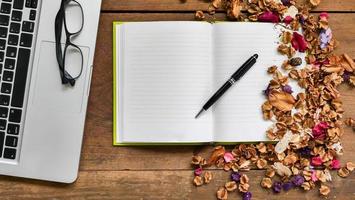 Top view workspace with notebook,pen,glasses,laptop and dried flowers on wooden table background . photo