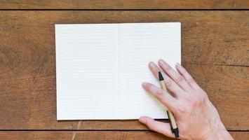 Man hands with pen writing on empty notepad over wooden table. photo