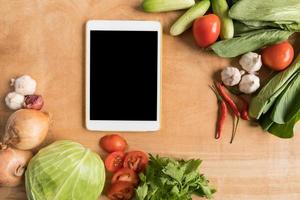 Top view of Fresh vegetables with tablet touch computer gadget on wooden table background. photo