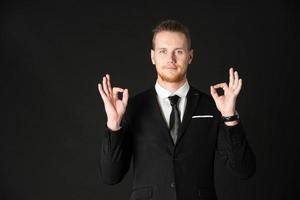 Portrait of handsome businessman in black suit showing okay symbol hand isolated on black background photo