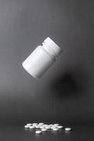 Unlabelled white plastic pill bottle. Poured out several small white pills. come out below in black background photo