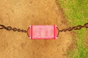 Take a top view of the red swing with chains in the playground. in the park saw the ground and the grass photo
