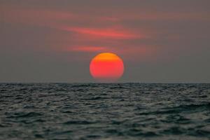 The sun is falling into the sea, the bottom of the sun eccentric because the refraction of the atmosphere. , The sky is orange And the sea is dark photo